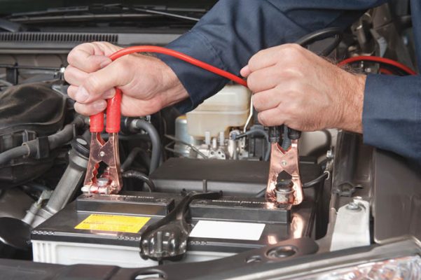 A car mechanic uses battery jumper cables to charge a dead battery.